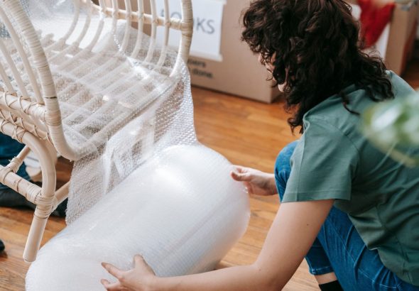 A mover carefully wraps an antique wooden table with protective padding inside a residential living room before a move.