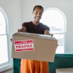 A mover carefully packs cardboard boxes in a bright, modern apartment living room, preparing for a residential move.