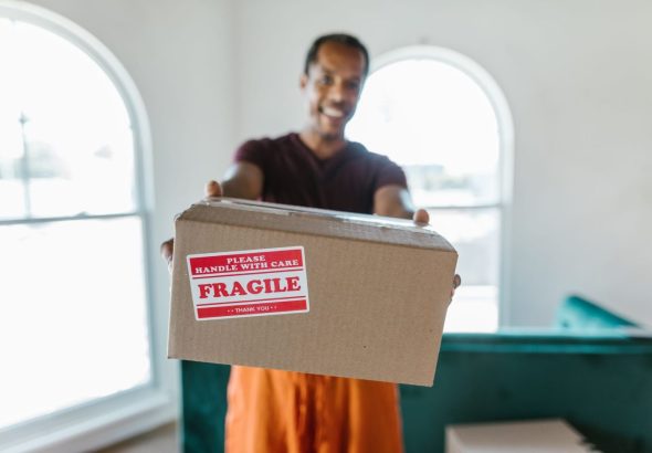 A mover carefully packs cardboard boxes in a bright, modern apartment living room, preparing for a residential move.