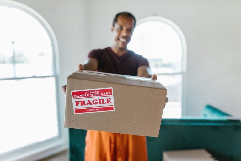 A mover carefully packs cardboard boxes in a bright, modern apartment living room, preparing for a residential move.