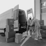 A mover carries a cardboard box toward a moving truck parked outside a residential home.