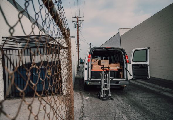Movers carrying furniture and boxes into a moving truck parked in front of a house on a sunny day.