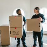 Movers carefully wrapping a grand piano with protective blankets inside a residential living room before a move.