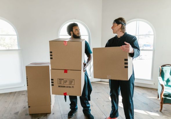 Movers carefully wrapping a grand piano with protective blankets inside a residential living room before a move.